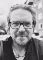 Black-and-white headshot of Martin, glasses and short beard, smiling outdoors